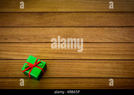 Metallic green gift package with red ribbon on a wooden background. Stock Photo