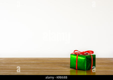 Metallic green gift package with red ribbon on a wooden table against a white background. Stock Photo