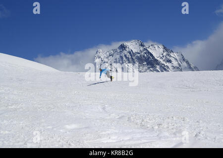 Snowboarder downhill in high snowy mountains at sun winter day. Caucasus Mountains, region Dombay. Stock Photo