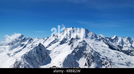 Panoramic view of snow covered mountain peaks and beautiful blue sky with clouds at sun windy day. Caucasus Mountains in winter, region Dombay. Stock Photo