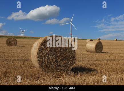 stubble with hay bales and wind turbines in the background against blue sky white clouds Stock Photo