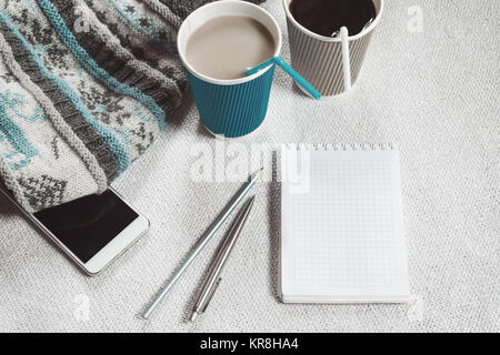Coffee in paper cups, knitted scarf and phone on a white table. In blue tones Stock Photo