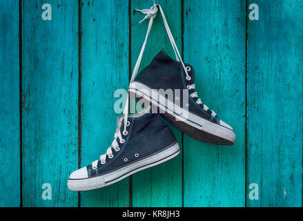 pair of blue men's sports sneakers hanging from a nail on the wall of the old shabby green Stock Photo