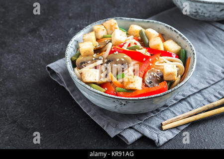 Stir fry with udon noodles, tofu, mushrooms and vegetables. Asian vegan vegetarian food, meal, stir fry over black background close up. Stock Photo