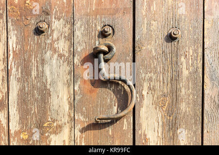 Rusty hook hanging on peeling wooden background. Close up view. Stock Photo