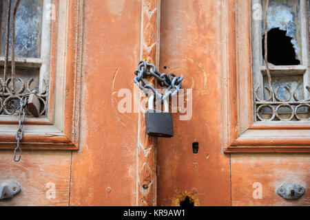 Rusty lock on a destroyed wooden entrance with broken window. Close up view with details. Stock Photo