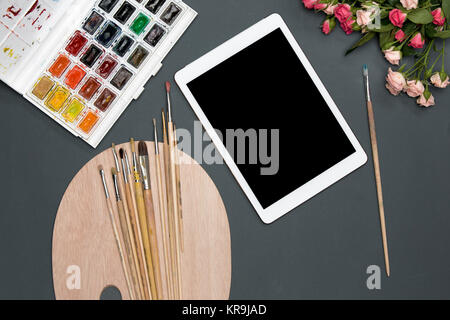 The workspace of artist with laptop, paints, paintbrushes, flowers on black Stock Photo