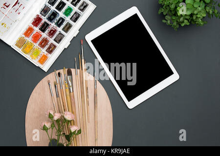 The workspace of artist with laptop, paints, paintbrushes, flowers on black Stock Photo