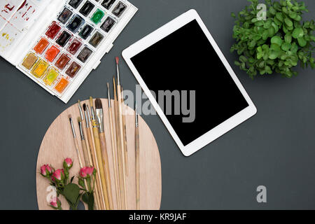 The workspace of artist with laptop, paints, paintbrushes, flowers on black Stock Photo