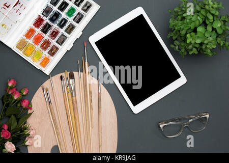 The workspace of artist with laptop, paints, paintbrushes, flowers on black Stock Photo