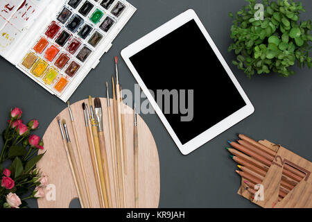 The workspace of artist with laptop, paints, paintbrushes, flowers on black Stock Photo
