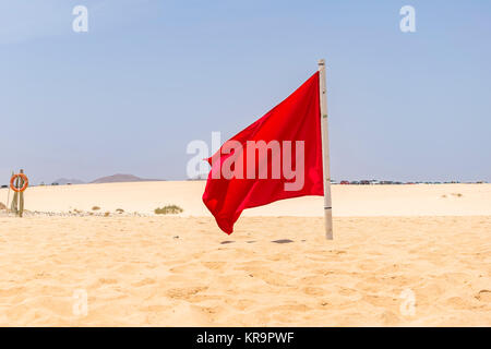 Red flag flying in the wind on the beach Stock Photo