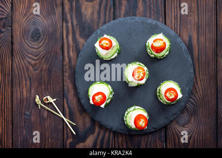 Appetizer canape with white bread, feta cheese, cucumber and cherry tomatoes on a wooden table. Stock Photo