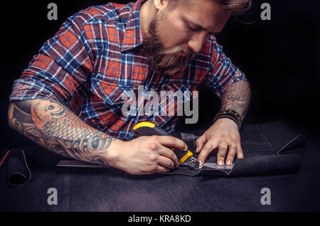 Currier producing a leatherwork at his workshelf./Craftsman works with leather goods in his tanner shop. Stock Photo