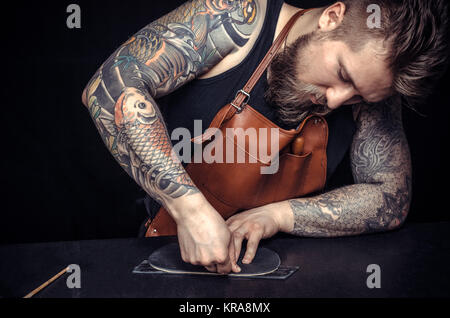 Worker of leather makes quality products at his tanner shop./Craftsman performing leatherwork on a new product piece . Stock Photo