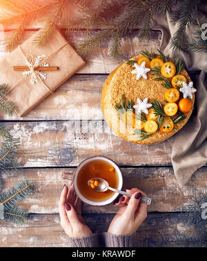 Christmas Honey cake on the table. Woman holding tea with berry near decorated present at breakfast. Stock Photo