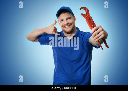 plumbing services - plumber with wrench showing phone call gesture on blue background Stock Photo