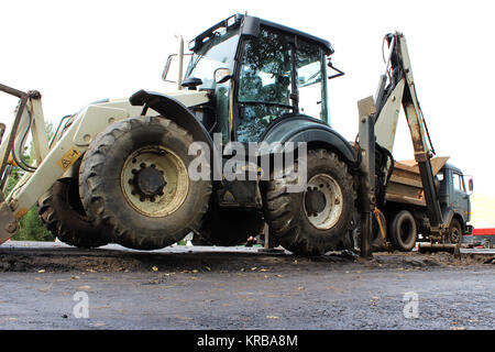 Truck strong outrigger stabilizing legs extended. Tractor on extended outriggers for better stability, digging a bucket of road for repair. reportage photography. Stock Photo