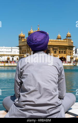 Vertical picture of Sikh man praying in front of the lake at Sri Harmandir Sahib, known as Golden Temple, located in Amritsar, Punjab, India. Stock Photo