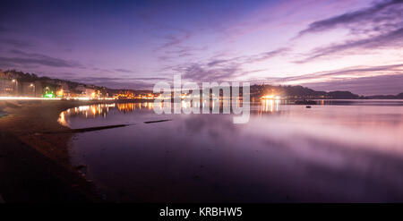 The lights of Oban town are reflected in the sea water along the sweep of Oban Bay at sunset in the Argyll district of the west Highlands of Scotland. Stock Photo