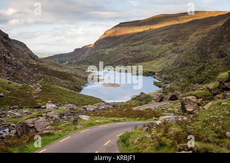 A narrow lane winds through the mountain pass and past Augher Lake in the Gap of Dunloe, nestled in the Macgillycuddy's Reeks mountains in Ireland's C Stock Photo