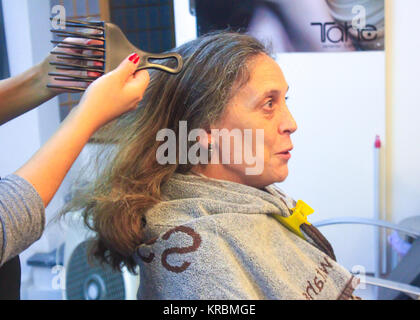 Stylist hold a comb ready to comb a mature lady with long hair sitting a salon chair and covered with a towel preid with a yellow spring Stock Photo