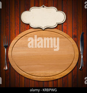 Wooden oval cutting board with empty label and silver cutlery, fork and knife on wooden table Stock Photo