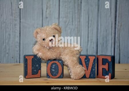 white teddy bear lies on cubes with the word love in front of white wooden wall Stock Photo