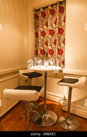A portrait image of the corner of a bar with a table and three chairs with a wine bottle and two glasses. February 2016 Stock Photo