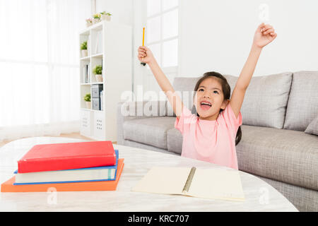 cheerful beauty girl kid raised hands up celebrating her school studying homework finally finished during holiday at home before back to school. Stock Photo