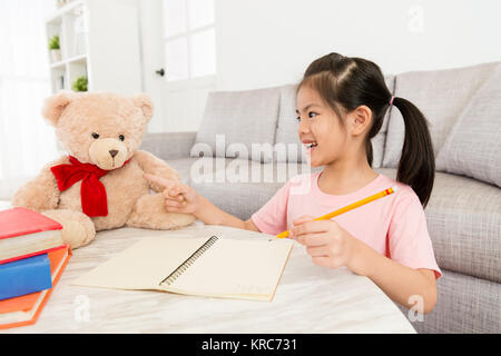 happy lovely girl children teaching her teddy toy learning english at home when she doing school homework in living room. Stock Photo