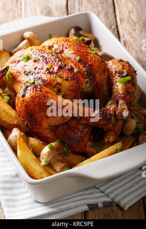 Appetizing baked chicken with mushrooms and potatoes close-up in a baking dish on a table. vertical Stock Photo
