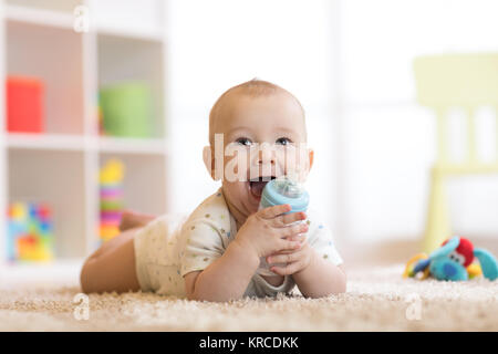 Pretty baby boy drinking water from bottle. Smiling child is 7 months old. Stock Photo