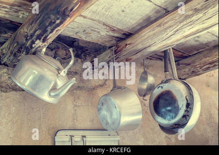 Old kitchen utensils in aluminum. Hanging from old wooden beams, pans, strainer, kettle.  Photo in styles vintage Stock Photo