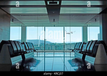 An empty modern airport departure lounge with seating and plane taking off in the background Stock Photo