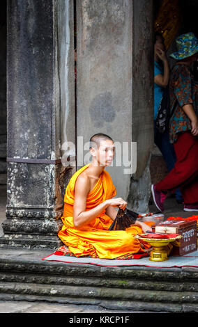 Young Buddhist monk in saffron robes sits in Angkor Wat, a temple complex near Siem Reap in Cambodia, the largest religious monument in the world Stock Photo