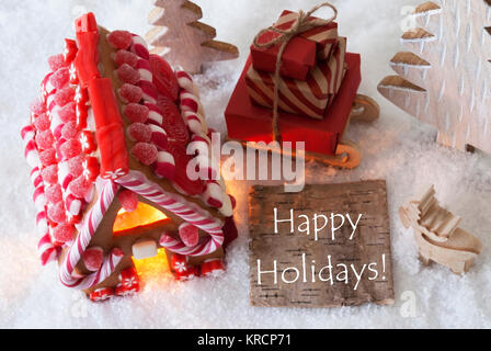 label with english text happy holidays. gingerbread house on snow with christmas decoration like trees and moose. sleigh with christmas gifts or presents. Stock Photo