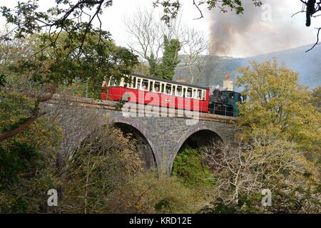View of the Snowdon Mountain Railway crossing a bridge at Waterfall Halt just above the town of Llanberis in Gwynedd, North Wales.  From Llanberis Station the train passes the waterfall and begins the steep climb to the top of Snowdon.  Passengers can be seen inside the carriage, looking out at the scenery. Stock Photo