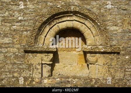 Norman architectural detail embedded in a wall of All Saints Church in the village of Turkdean, Cotswolds, Gloucestershire. Stock Photo