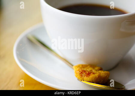 Coffee cup and saucer with brass spoon and cookie on wooden table. Modern cafeteria stylish espresso setting with gold colored teaspoon and biscuit ap Stock Photo