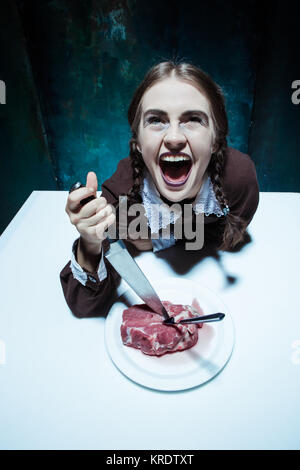 Bloody Halloween theme: crazy girl with a knife, fork and meat Stock Photo