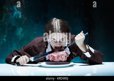 Bloody Halloween theme: crazy girl with a knife, fork and meat Stock Photo