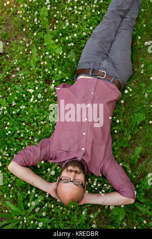 Bald man puts his arms behind his head to relax on some green grass in the Summer in Oregon at a park. Stock Photo