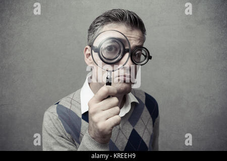 Nerd guy looking through a magnifying glass with a clueless expression Stock Photo