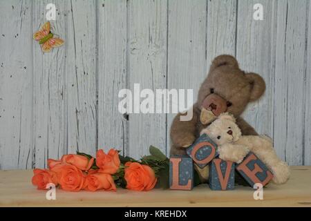 two teddy bears with roses and love lettering against white wooden wall Stock Photo