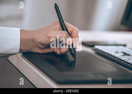 Graphic designer's workspace. Hand on pen tablet. Young smart man in the office. Free black monitor copy space for design. Stock Photo