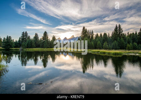 Sunlight creeps behind peaks of Teton Mountain Range with glassy water in the foreground, Grand Tetons National Park, Teton County, Wyoming Stock Photo