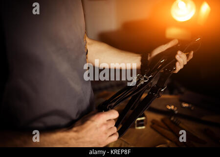 Working process of the leather craft in the workshop. Man holding photographer's belt for camera.Wooden background. Tanner in old tannery.Close up arm Stock Photo