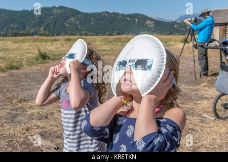 Two young girls look up wearing eclipse glasses to watch Solar Eclipse, Grand Tetons National Park, Teton County, Wyoming Stock Photo