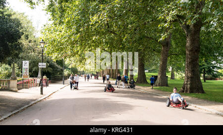 People riding recumbents trike bikes or walking along the pedestrian avenue enjoying the good weather in Battersea Park, London, UK Stock Photo